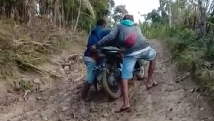 Dua pengendara sedang mendorong sepeda motor melewati tanjakan berlumpur di salah satu titik jalan  Nanin -,Nanebot yang rusak berat.