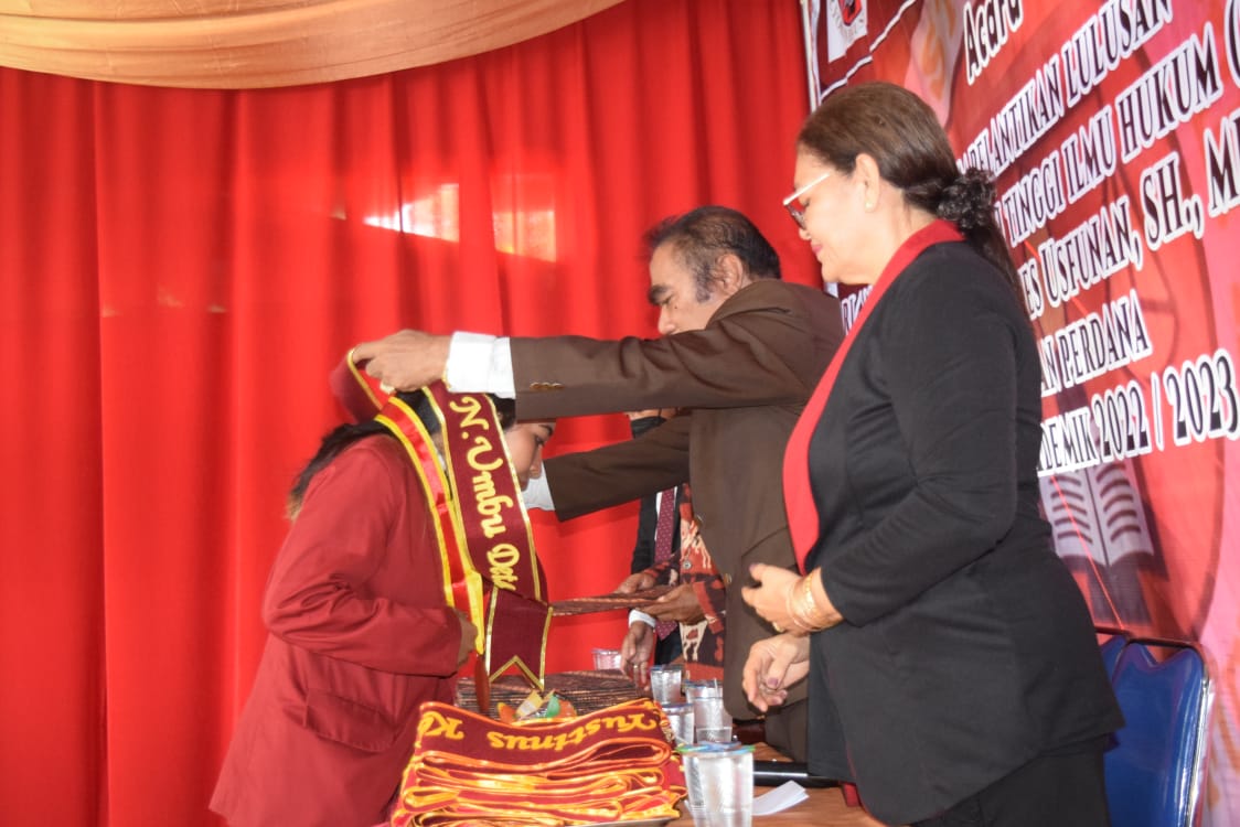 Direktur STIKUM, Prof.Dr.Yohanes Usfunan, SH.MH, sendang menyematkan selempang kelulusan untuk salah satu lulusan STIKUM. Foto: istimewa.